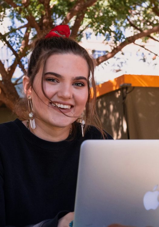 A young woman sitting in front of a laptop, looking at the camera